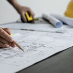 A close-up, an architect, a house designer holding a pencil, pointing to a house plan to examine the design plan before discussing the details with the client. Interior design and decoration ideas.