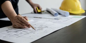 A close-up, an architect, a house designer holding a pencil, pointing to a house plan to examine the design plan before discussing the details with the client. Interior design and decoration ideas.